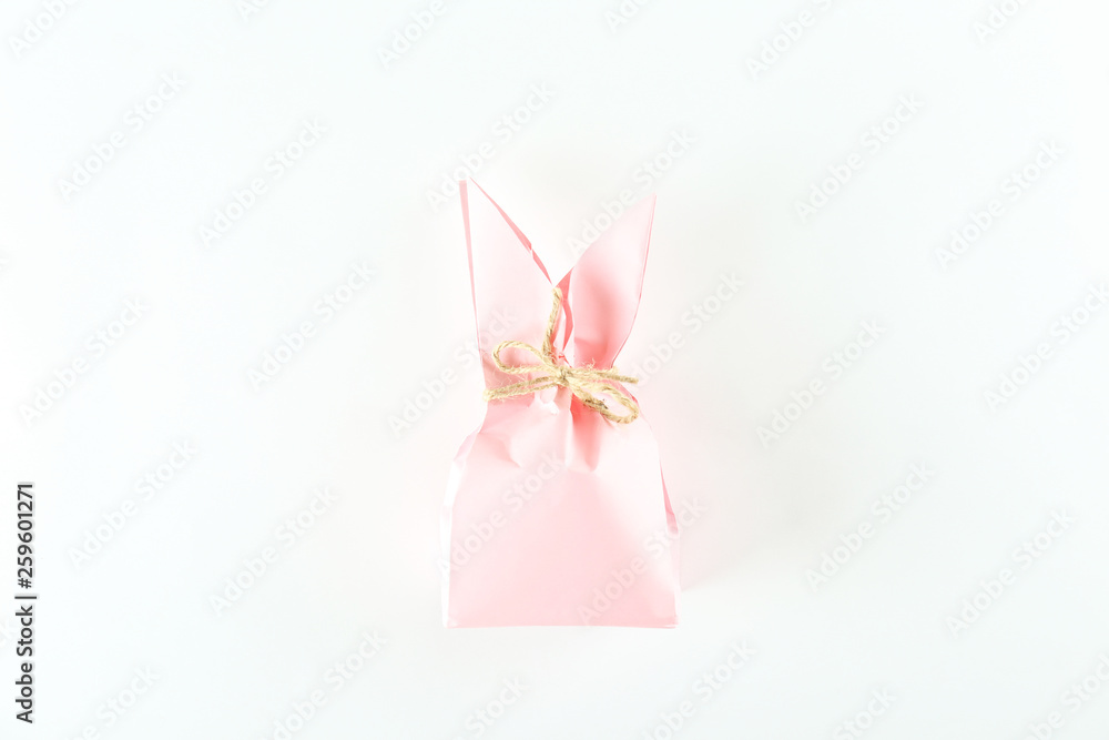 Pink Easter present box in a form of bag with bunny ears in minimal top view composition with bright paper background. A lot of copy space for text. Close up, flat lay.