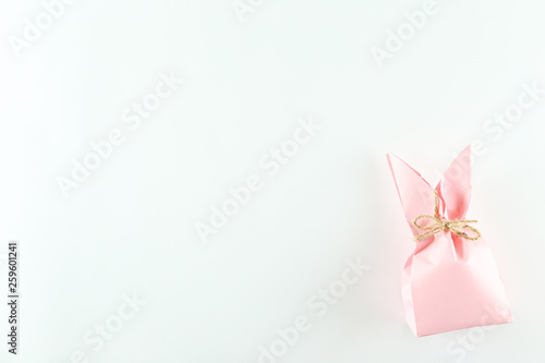 Pink Easter present box in a form of bag with bunny ears in minimal top view composition with bright paper background. A lot of copy space for text. Close up, flat lay.