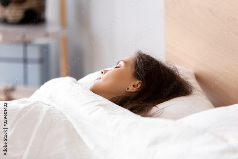 Young woman sleeping on bed covered with white blanket Young woman sleeping on bed covered with white blanket