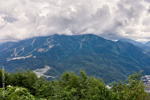 Sports facilities and residential buildings on the slope of a high mountain with a green slope and the top in the clouds. A sports and tourist base in the mountains.