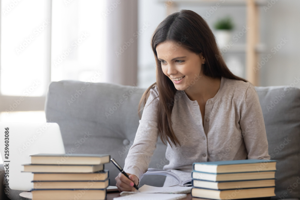 Positive student girl sitting on couch at table and studying Positive student girl sitting on couch at table and studying