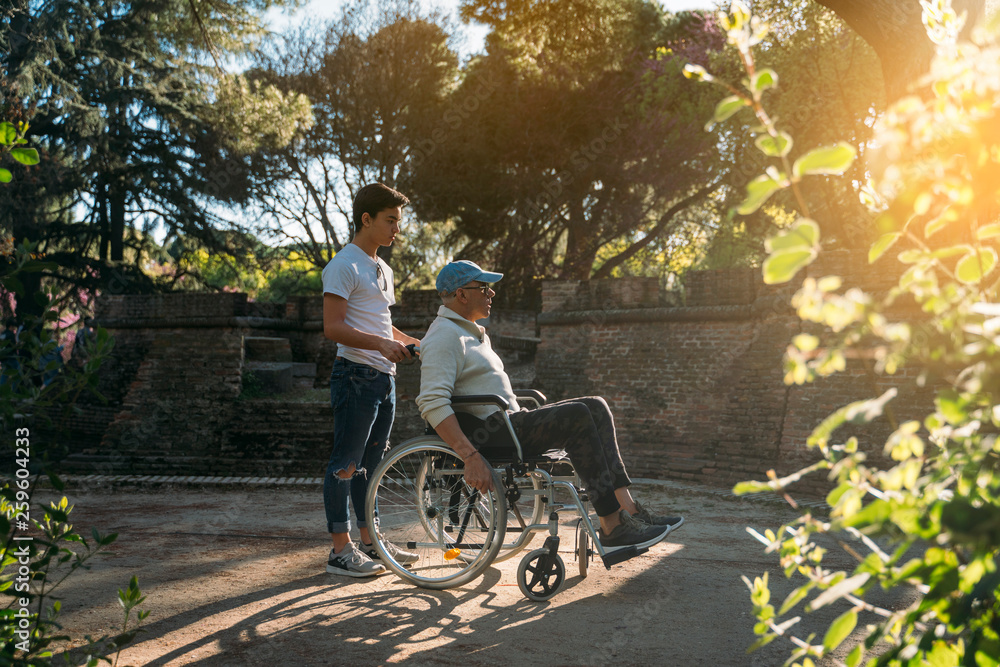 Obraz premium 56 year old male sitting on a wheelchair and he young friend in the park