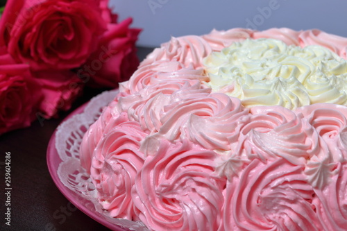 Biscuit cake, decorated with a cream with shades of pink. Nearby is a bouquet of roses.