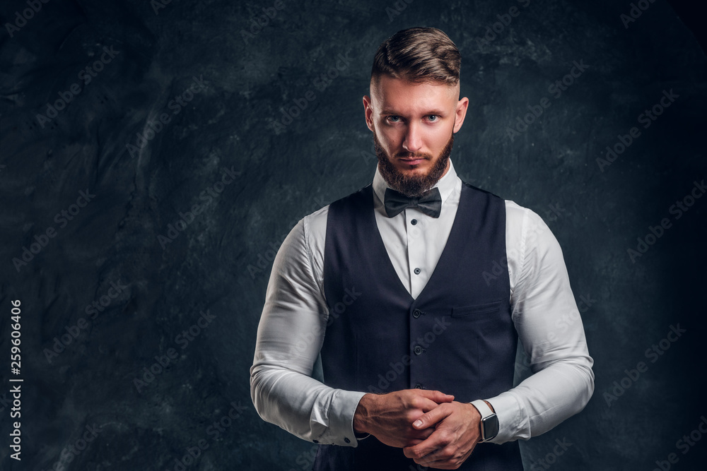 Elegantly dressed bearded hipster in a vest with bow tie. Studio photo against a dark wall background Elegantly dressed bearded hipster in a vest with bow tie. Studio photo against a dark wall background