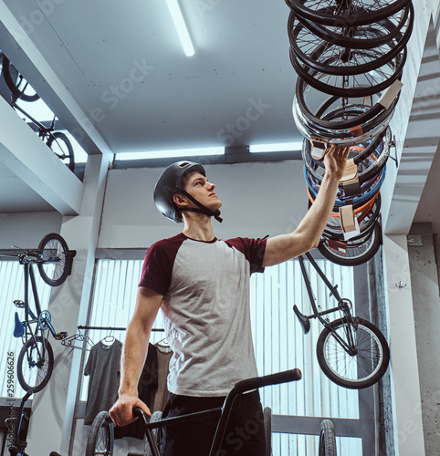 Young man in a protective helmet and choosing bicycle tire for his bike in the shop photo