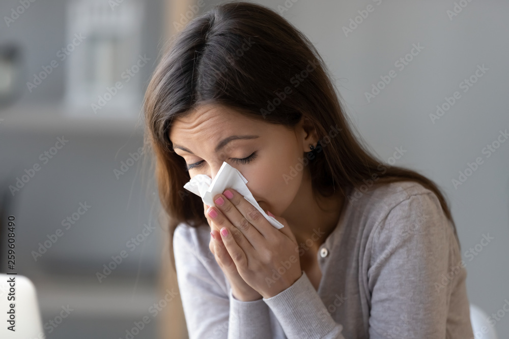 Sick young woman holding tissue and blowing her running nose Sick young woman holding tissue and blowing her running nose