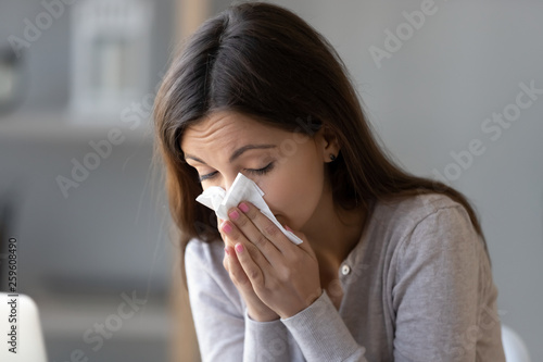 Sick young woman holding tissue and blowing her running nose