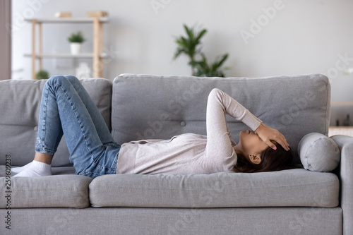 Full length young woman lying on couch suffers from heartache