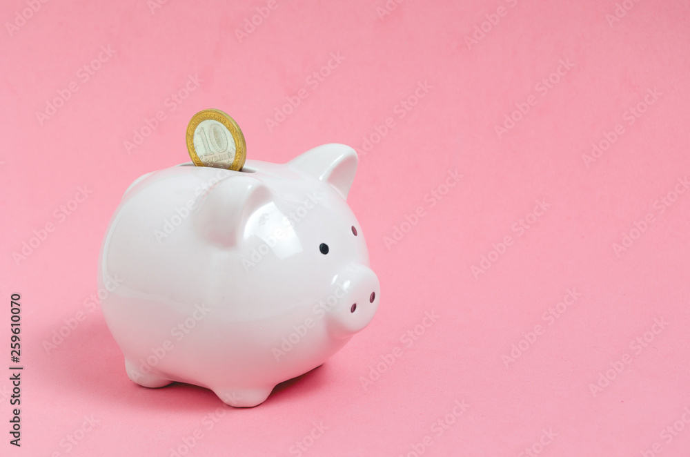Coin falls into pink, porcelain piggy Bank on pink background.