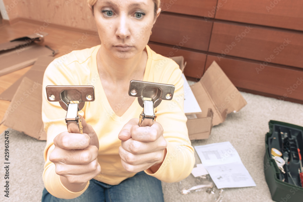 Single young woman assembling pieces of new furniture and holding two