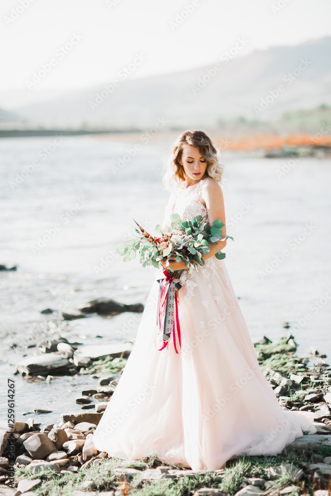 Beautiful fashion bride in wedding dress posing near river
