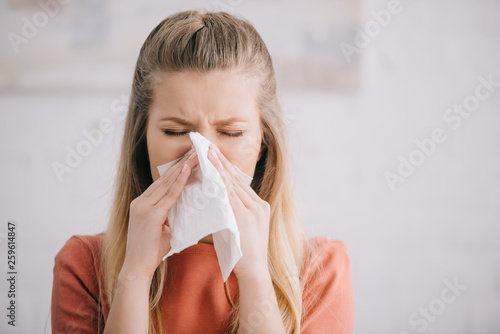 close up of blonde woman sneezing in tissue at home