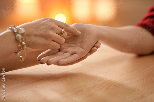 Chiromancer reading lines on woman's palm at table, closeup photo