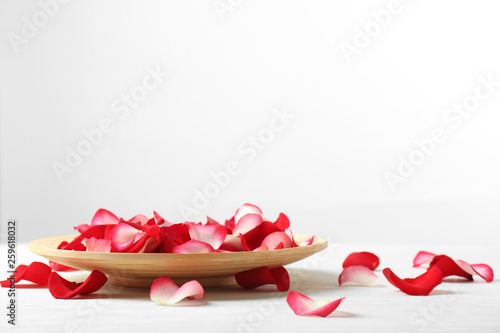 Wooden plate with rose petals on table against white background. Space for text
