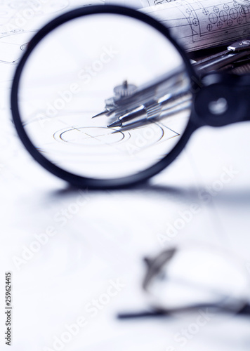 View of a compass through a magnifying glass on the background of a roll with drawings