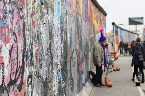 Close-up of graffiti at the East Side Gallery, section of the Berlin Wall in Berlin, Germany. Street musician and tourists in the background.