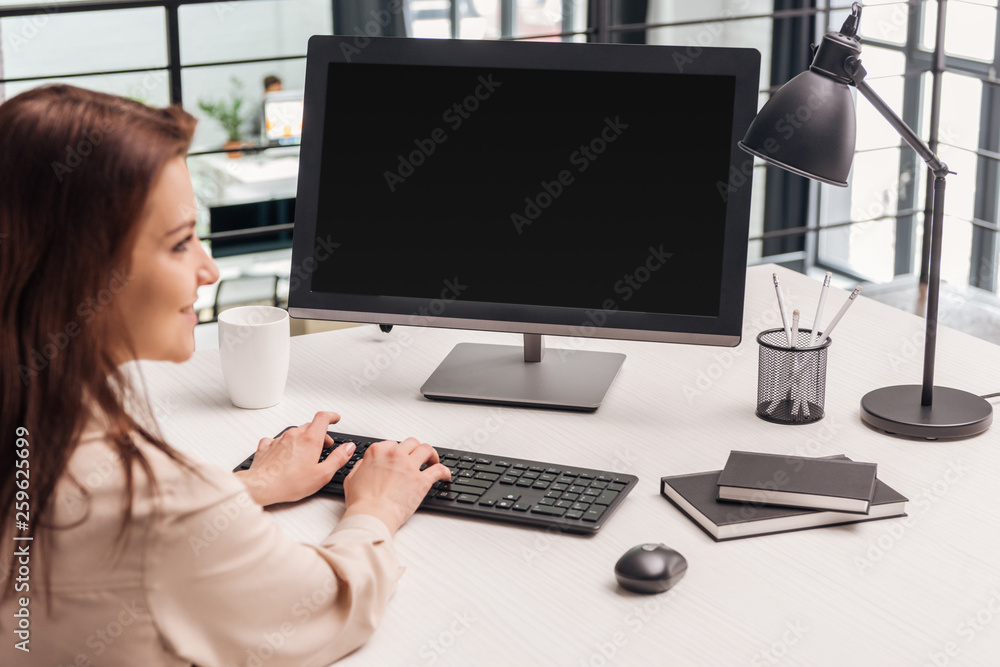 selective focus of smiling woman using computer at workplace