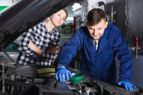 Two masters are replacing the oil in the car in workshop.