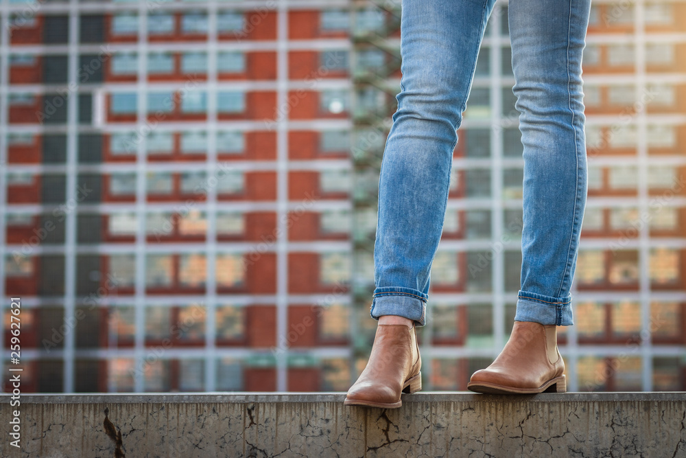 Female legs in jeans and leather shoe. Stylish woman standing in city. Modern architecture background