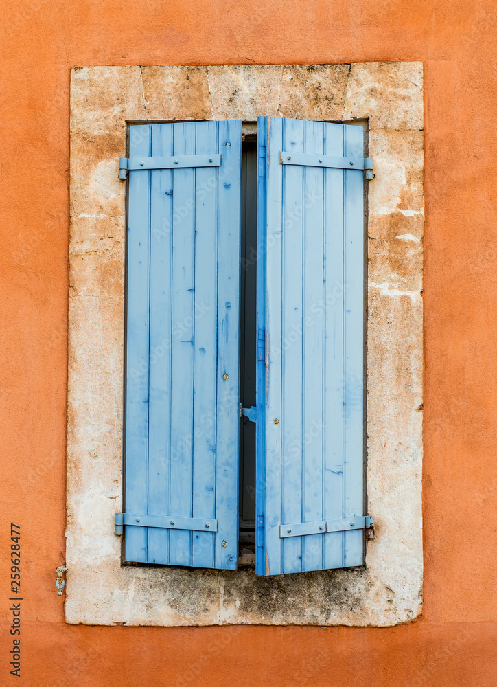 Naklejka premium stara niebieska drewniana okiennica na pomarańczowej ścianie - Roussillon, Prowansja, Francja