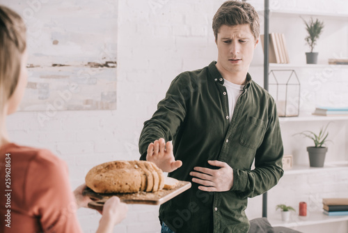 cropped view of woman holding cutting board with sliced bread near handsome man with gluten allergy photo