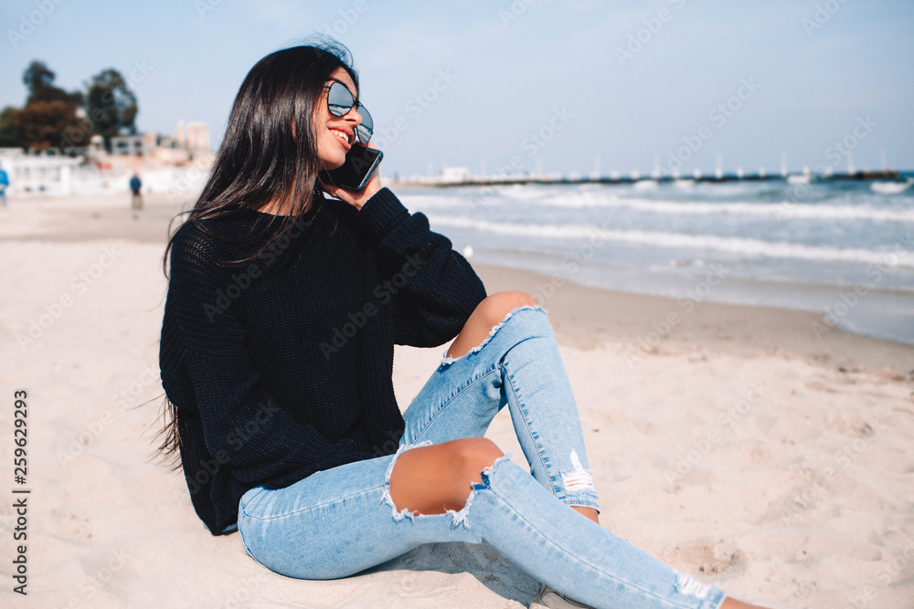Young woman talking on mobile phone on a beach with ocean sea background.nice smile beautiful middle age lonely woman enjoy the beach sitting on a seat with ocean in background. using smartphone 