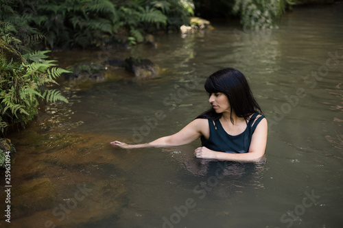 Beautiful Azorian woman walking through water in hot spring water of Caldeira Velha between ferns and foliage. 