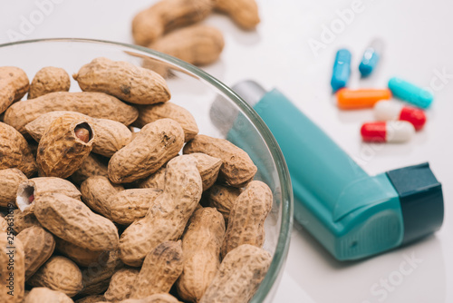 selective focus of glass bowl with tasty peanuts near pills and blue inhaler on grey