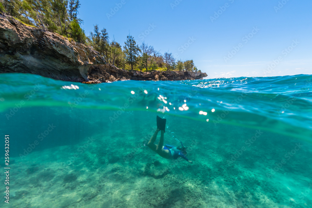 Snorkeler swimming under cliffs in clear blue water