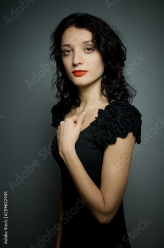 Portrait of amazing young brunette woman with red sensual lips posing on black background in studio and touching her neck.