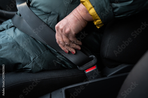 Older senior woman fastens a safety belt in a car wearing green and yellow jacket