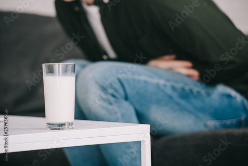 selective focus of glass of milk on coffee table near man holding stomach