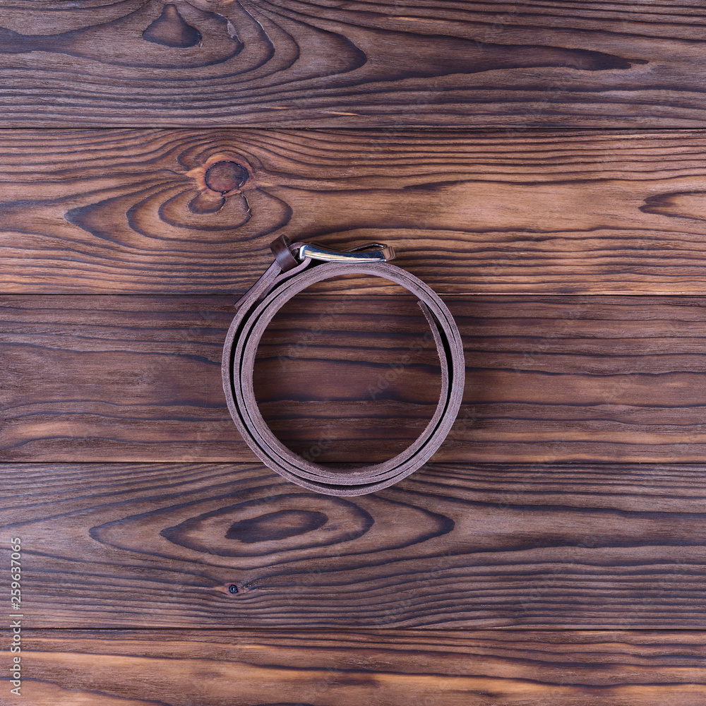 Brown color handmade belt lies on textured wooden background. The belt is twisted into a ring. Up to down view. Stock photo of businessman accessories. Brown color handmade belt lies on textured wooden background. The belt is twisted into a ring. Up to down view. Stock photo of businessman accessories.