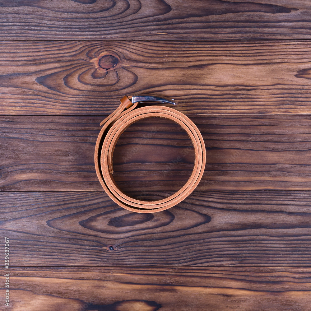 Hue ginger color handmade belt lies on textured wooden background. The belt is twisted into a ring. Up to down view. Stock photo of businessman accessories. Hue ginger color handmade belt lies on textured wooden background. The belt is twisted into a ring. Up to down view. Stock photo of businessman accessories.