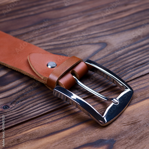 Hue ginger color handmade belt buckle lies on textured wooden background closeup. Side view. Stock photo of businessman accessories.