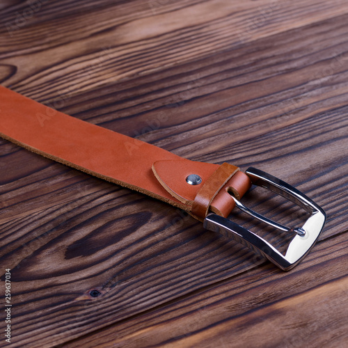 Hue ginger color handmade belt buckle lies on textured wooden background closeup. Side view. Stock photo of businessman accessories.