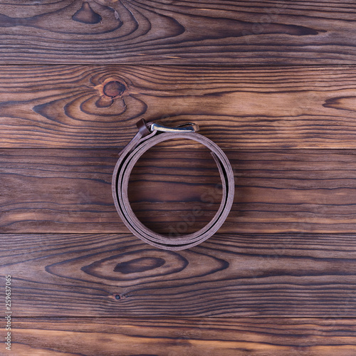 Brown color handmade belt lies on textured wooden background. The belt is twisted into a ring. Up to down view. Stock photo of businessman accessories.