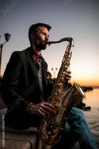 A musician with a hanger sits on the waterfront in the evening at sunset against the background of the night city