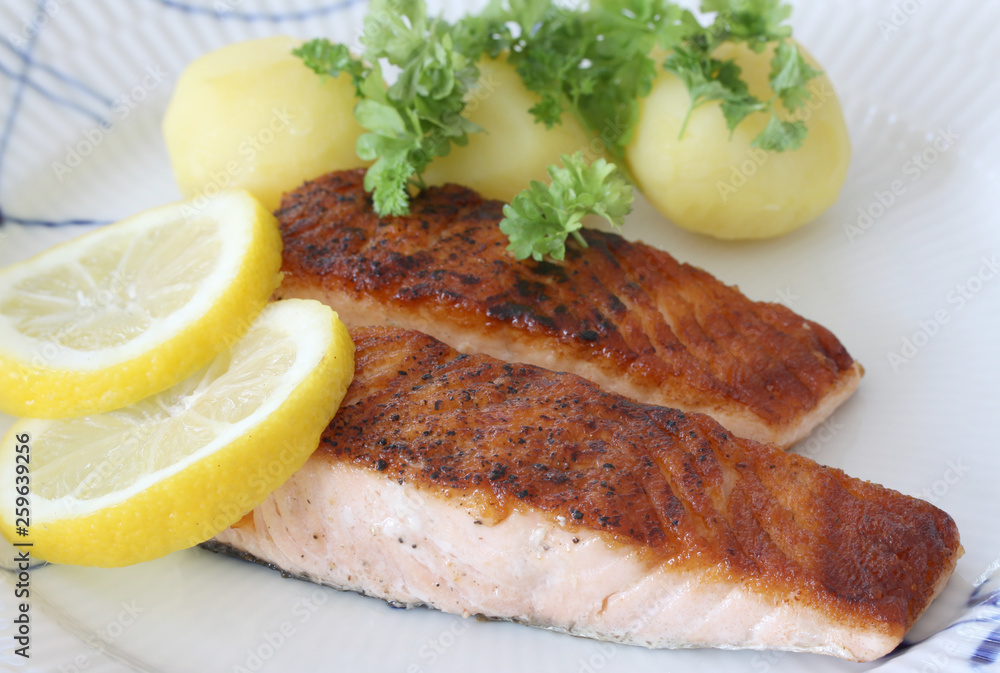 Grilled salmon fish filets on a plate with Potatoes, parley and slices of lemon. Close up stock photo with white background. Grilled salmon fish filets on a plate with Potatoes, parley and slices of lemon. Close up stock photo with white background.