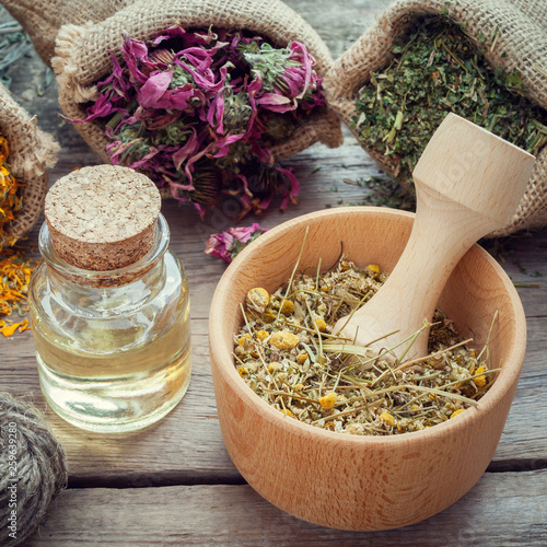 Fotografie Medicinal herbs in hessian bags, wooden mortar of dry chamomile buds and essential oil on wooden table, herbal medicine