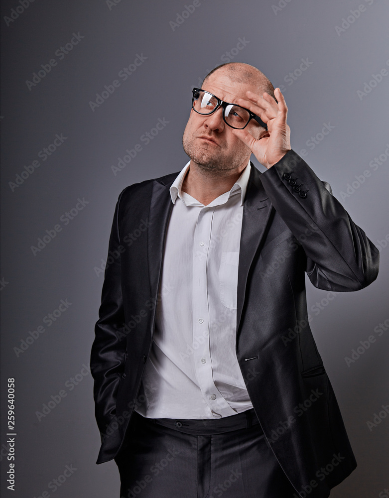 Fototapeta premium Thinking bald business man looking up serious in eyeglasses and have an idea in suit on grey background. Closeup