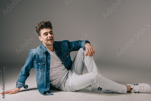 smiling handsome man in denim shirt and jeans sitting on floor and looking at camera