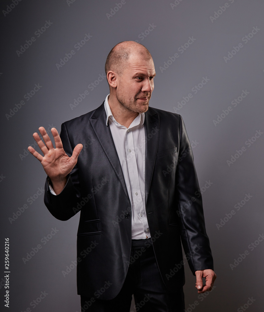 Unhappy depressed bald busuness man in black suit showing the palm stop sign on grey background. Closeup Unhappy depressed bald busuness man in black suit showing the palm stop sign on grey background. Closeup