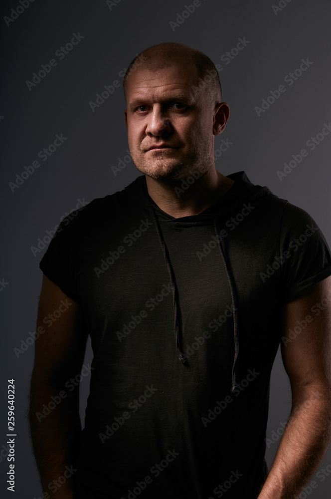 Depression angry crime man with bald head looking mystery and agressive in black shirt on dark grey background. Closeup