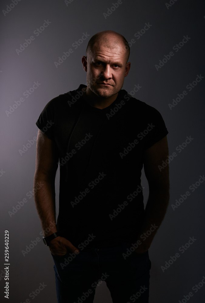 Sad angry crime man with bald head looking mystery and agressive in black shirt on dark grey background. Closeup