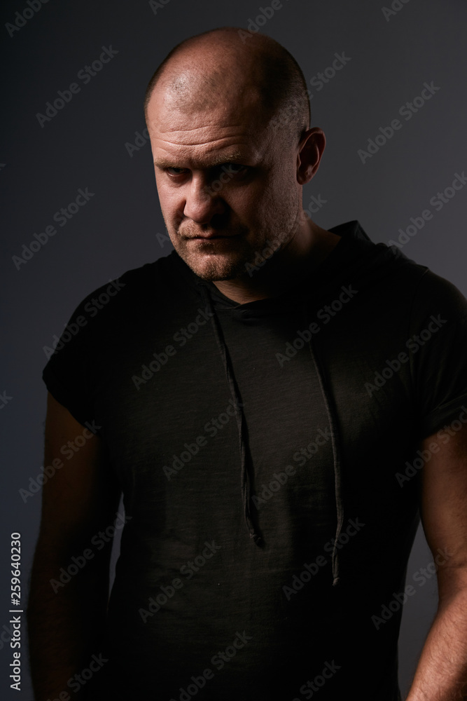 Sad angry crime man with bald head looking mystery and agressive in black shirt on dark grey background. Closeup