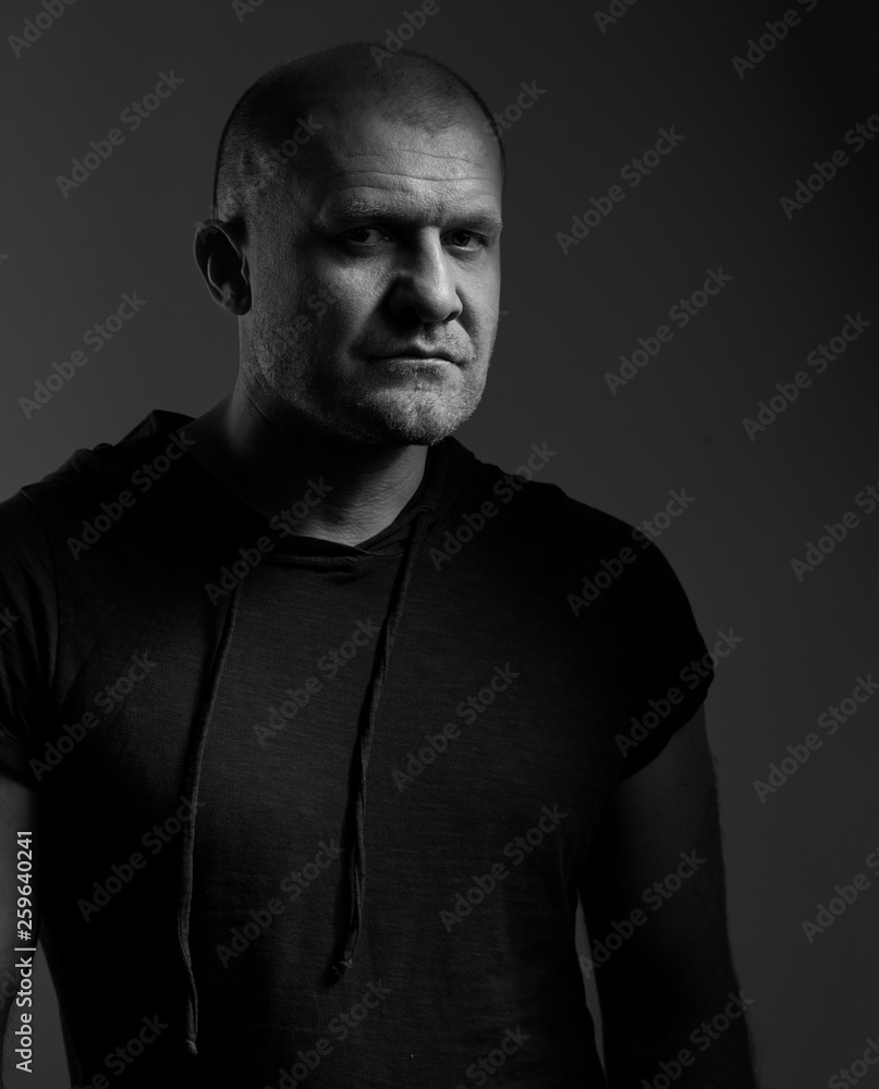 Naklejka premium Sad angry crime man with bald head looking mystery and agressive in black shirt on dark grey background. Closeup