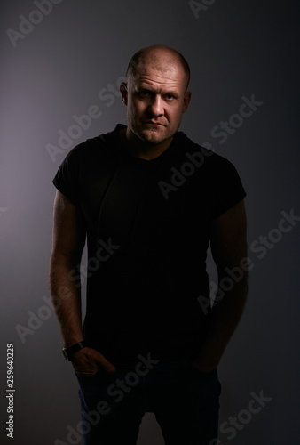 Sad angry crime man with bald head looking mystery and agressive in black shirt on dark grey background. Closeup © nastia1983