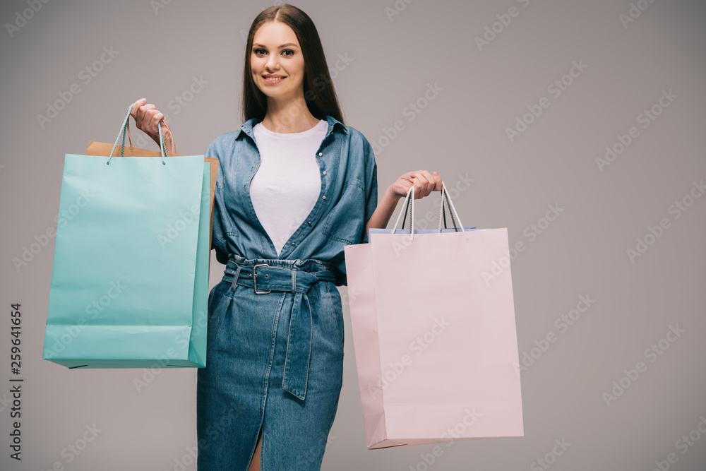 smiling and beautiful woman in denim dress holding shopping bags and looking at camera