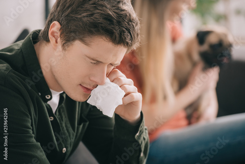selective focus of handsome man allergic to dog holding tissue while sitting with girl and pug
